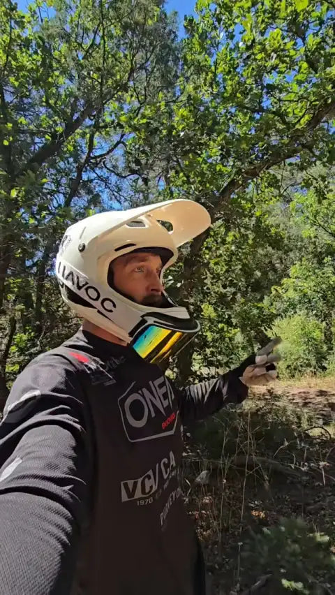 Rider in a white full-face helmet and riding jersey on a wooded trail
